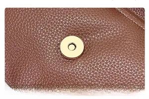 Macro view of golden round magnetic clasp on brown lychee texture leather bag