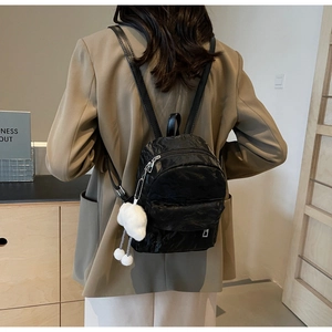 Detail of black mini backpack with pleated texture and white cloud plush pendant