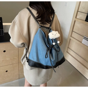Detail of blue denim backpack with black leather trim and white cloud charm accessory