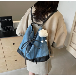 Detail of blue denim backpack with leather base, bow decor, and cloud plush charm