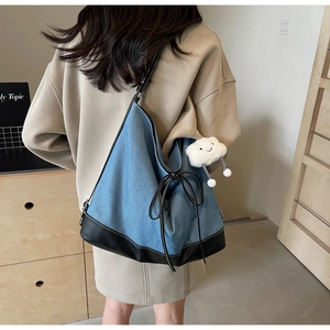 Detail of blue denim tote bag with black leather bottom and cute plush cloud charm