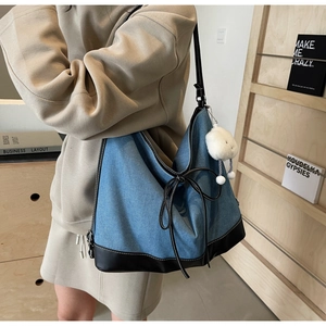 Detail of blue denim tote bag with black leather straps and plush white ball charm
