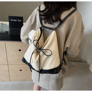 Detail of canvas backpack featuring black bow decoration and plush pendant attachment