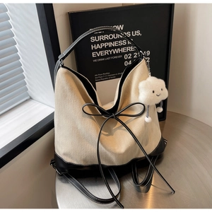 Detail of canvas tote bag with black leather trim and white plush cloud charm on table