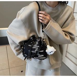 Detail of black drawstring bucket bag with wavy pink embroidery and white plush lamb charm