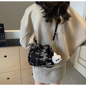 Detail of black drawstring bucket bag with white wave embroidery and plush charm pendant