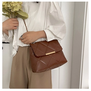 Detail of dark brown quilted crossbody bag with gold hardware on white shirt outfit