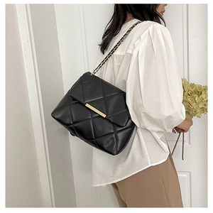 Macro detail of black quilted texture and golden chain strap on a stylish crossbody bag