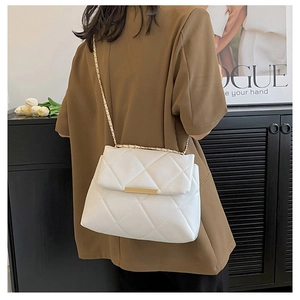 Close-up of white quilted chain bag with gold metal trim worn by model in a chic setting