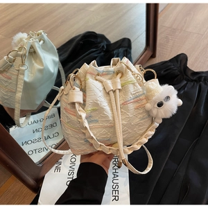 Detailed shot of cream bucket bag with colorful stitching, drawstring and plush charm