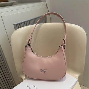 Sac bandoulière demi-lune rose avec nœud argenté posé sur une chaise moderne