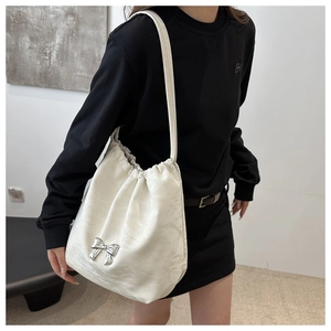 Détail du sac seau plissé blanc avec nœud en métal argenté sur fond de sweat à capuche noir