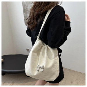 Détail du sac à cordon crème avec tissu texturé et accent de nœud papillon argenté