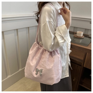 Détail du sac à bandoulière plissé rose avec un nœud argenté porté par un mannequin