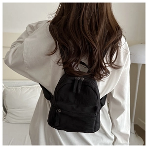 Back view of a black mini nylon backpack worn by a model in a cozy indoor setting