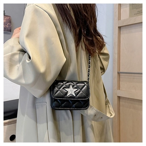 Detail of black quilted shoulder bag with silver star and chain strap on trench coat