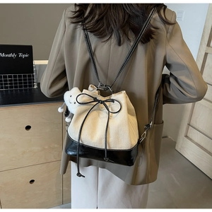 Close-up of cream canvas drawstring bucket bag with black leather base and plush charm