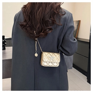 Detail of gold quilted mini crossbody bag with star emblem worn over a dark blazer