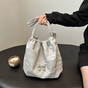 Sac fourre-tout argenté à texture froissée avec un nœud 3D sur une surface noire