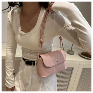Détail d'un sac carré rose avec nœud argenté et bandoulière nouée porté par un mannequin