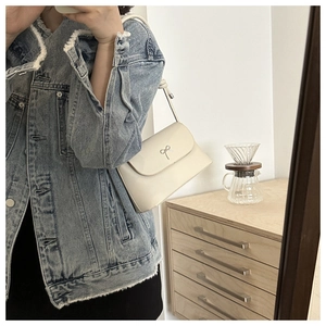 Détail d'un sac à bandoulière en cuir crème avec un nœud métallique argenté chic