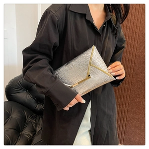 Detail of silver crocodile pattern envelope clutch with golden metal trim held by a model