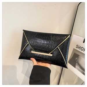 Detail of black crocodile pattern envelope clutch with gold metal trim and snap closure