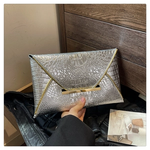 Detailed view of silver crocodile pattern envelope clutch with gold metal trim accents
