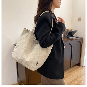Large capacity nylon tote bag in beige shown on shoulder in a modern office setting