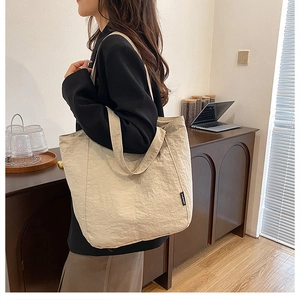 Détail d'un grand sac fourre-tout beige avec étiquette FASHION noire et tissu plissé