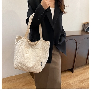 Close-up of cream nylon tote bag featuring crinkled texture and black fashion label detail