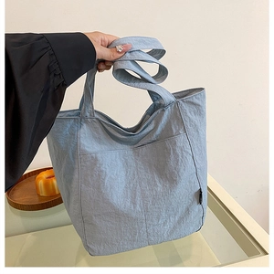 Detail of light blue nylon tote bag with front pocket shown in a lifestyle setting
