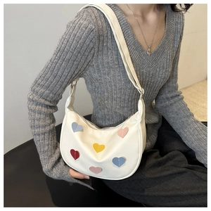 Model wearing a white half-moon crossbody bag with colorful heart patches and adjustable strap