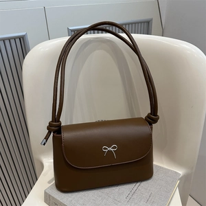 Petit sac rétro marron foncé avec nœud argenté posé sur un livre et chaise blanche