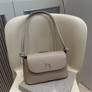 Sac bandoulière beige élégant avec nœud papillon en cuir de qualité sur chaise
