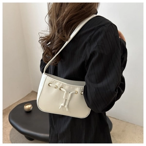 Detail of minimalist cream leather underarm bag featuring unique drawstring pleats and gold eyelets