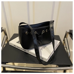 Detail of a black bucket bag with gold metal buckles and drawstring design on a chair