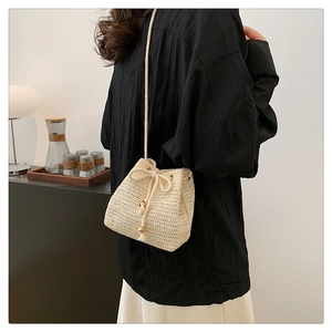 Detail of straw bucket bag with drawstring closure and golden bead accents worn by model