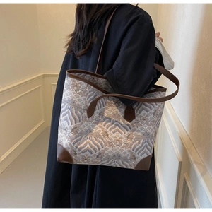 Close-up of a large-capacity beige tote bag with a wave pattern and dark brown leather trim