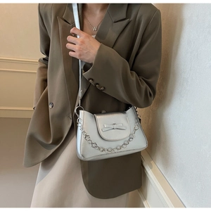 Detail of silver crossbody bag with metallic bow and floral chain on a model