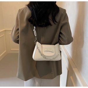 Detail of cream shoulder bag with bow and floral silver chain on model in suit