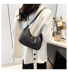 Close-up of black quilted leather crescent shoulder bag worn with a white blazer