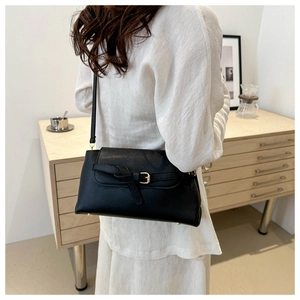 Close-up of minimalist black leather crossbody bag with buckle detail worn by a model