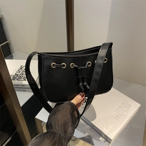 Minimalist black baguette bag with gold metal eyelets and decorative drawstring detail