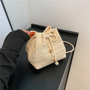 Handmade beige woven straw bucket bag with drawstring closure and wood bead detail