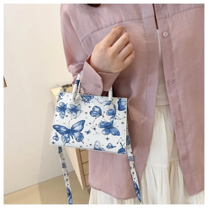 Close-up of white structured handbag with blue butterfly print and dual handles