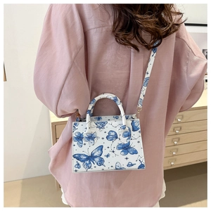 Detail view of printed crossbody bag featuring blue butterfly pattern on a pink shirt model