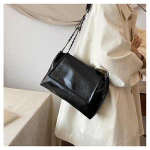 Détail d'un sac à bandoulière en cuir verni noir avec chaîne argentée et rabat élégant