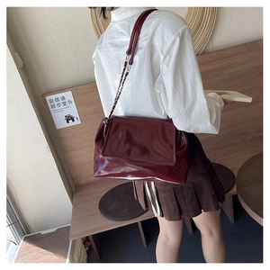 Détail d'un sac cabas en cuir verni bordeaux avec chaîne argentée porté à l'épaule