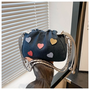 Détail d'un sac en denim foncé avec écussons cœurs colorés et bandoulière chaîne